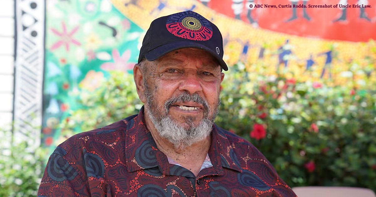 Portrait of Wakka Wakka Elder Uncle Eric Law, a smiling gently in front of a colourful mural at Cherbourg, South Burnett QLD