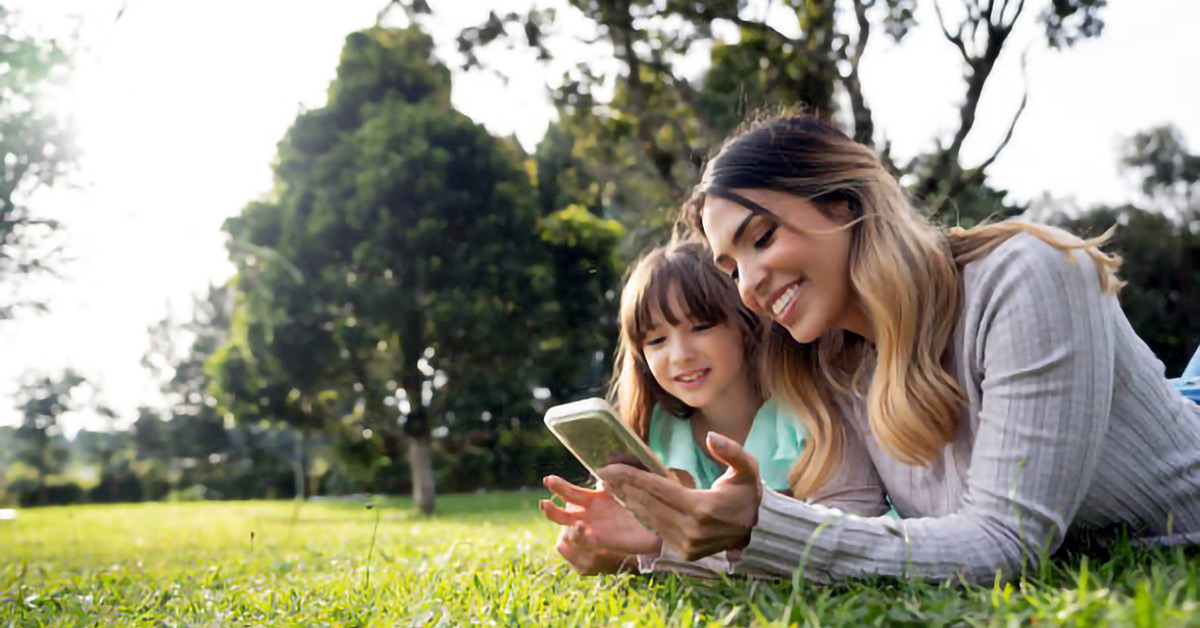 Mother and child lying on grass looking at a mobile phone together in the park