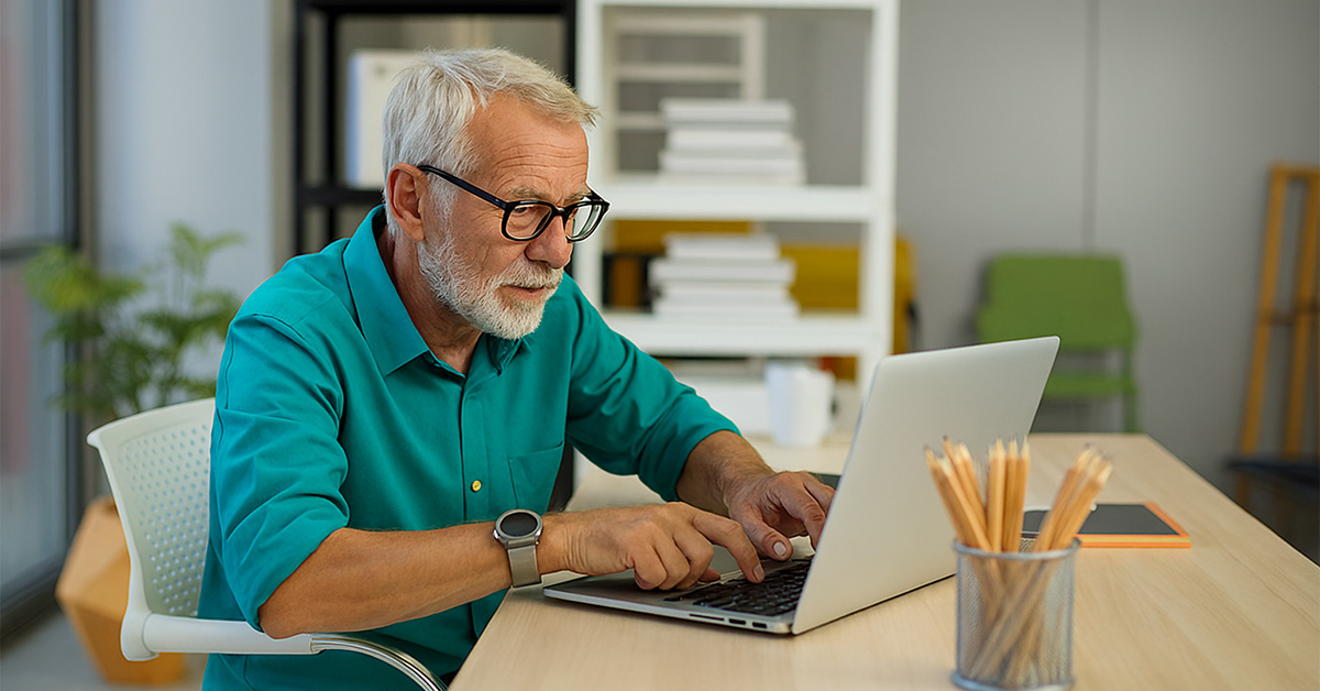 Older man sitting at desk struggling to navigate the internet on his laptop.